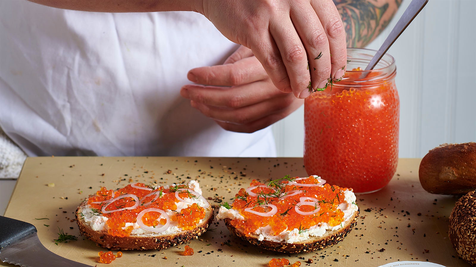 Loveski chef Christopher Kostow prepares a bagel with cream cheese, onion and orange roe.